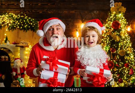 Santa Claus and child boy in room decorated for Christmas with present gift box. Winter holidays. Stock Photo