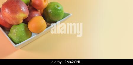 Fresh natural fruits in a white corner plate on a peach background. Peaches, nectarines, and limes. Card Stock Photo