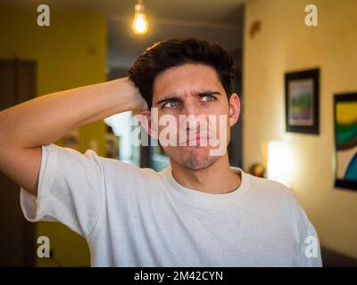 Confused or doubtful young man scratching his head and looking up Stock Photo
