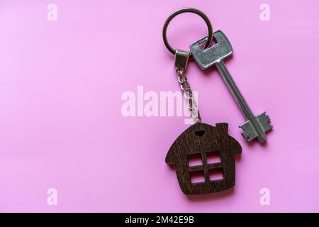 Key with a house keychain on a colored pink background. Real estate agent. Buying a house, apartment. Stock Photo