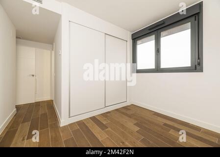 Empty room with a built-in wardrobe with white wooden sliding doors, black anodized aluminum windows and dark stoneware floors Stock Photo