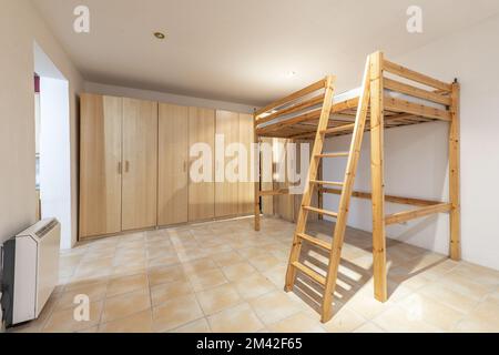 Room with a pine wood frame with stairs and box spring for a raised bed and a wall covered with wooden cabinets Stock Photo