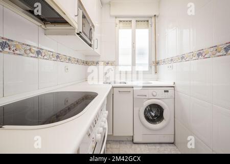 Kitchen with white furniture with counter and appliances of the same color and high border on the tiles Stock Photo
