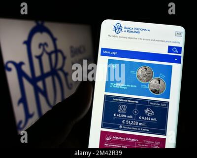 Person holding cellphone with website of central bank Banca Nationala a Romaniei (BNR) on screen with logo. Focus on center of phone display. Stock Photo