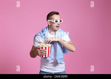 guy in 3d glasses eating popcorn on pink background Stock Photo
