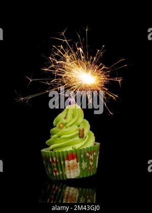 Fun Christmas style cupcake, cake with golden sparkler isolated on black background. Stock Photo