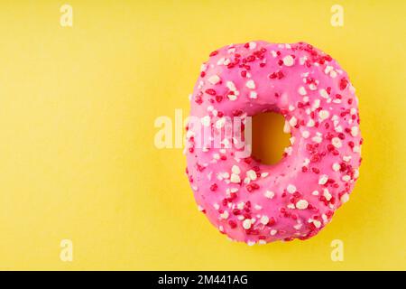 Strawberry donut with pink icing and sprinkles. Sweet pink donut on yellow background. Flat lay. Copy space Stock Photo