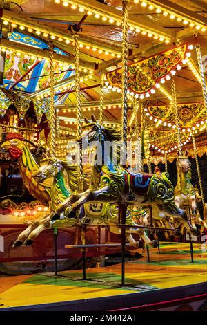 Brightly coloured fairground carousel with galloping ponies. At ...