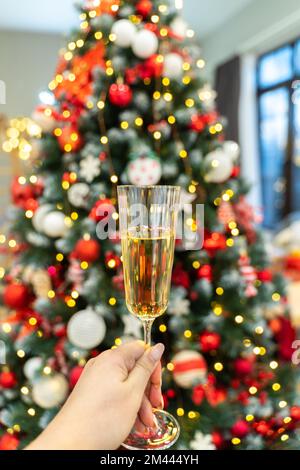 Champagne in a female hand against the background of Christmas tree lights. Selective focus. Festive day, atmospheric moment Stock Photo