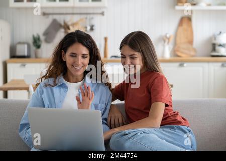 Happy family mother and daughter saying hello to relatives while making video call from laptop Stock Photo