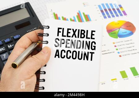 Finance and economics concept. The man is holding a pen and a notebook with the inscription - FLEXIBLE SPENDING ACCOUNT. In the background are financi Stock Photo