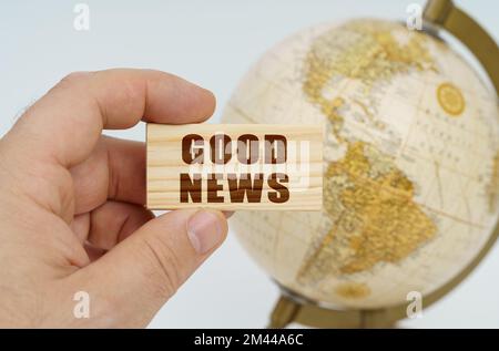 Globalization concept. A man holds in his hand a wooden plate on which it is written - GOOD NEWS. In the background is a globe. Stock Photo