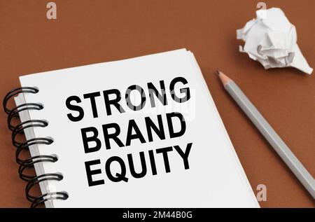 Business and finance concept. On a brown surface lies a pen, crumpled paper and a notepad with the inscription - STRONG BRAND EQUITY Stock Photo