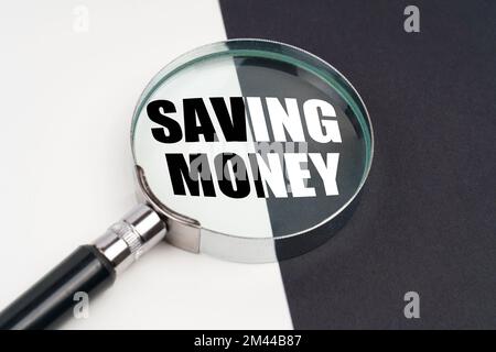 Business concept. On the surface, which is half black and white, lies a magnifying glass inside which is written - SAVING MONEY Stock Photo