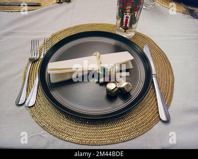 Gold Christmas bells on a black dinner plate setting with a gold metallic placemat Stock Photo