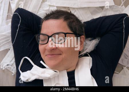 A closeup shot of a Caucasian short haired woman with glasses laying in a pile of white face masks Stock Photo