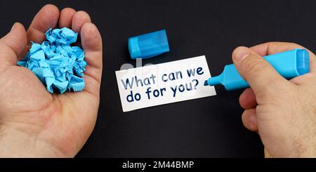 Business concept. In the hands of a man is blue crumpled paper and a marker, on a black table is a business card with the inscription - What can we do Stock Photo