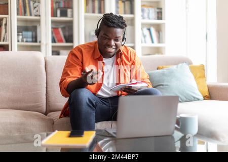 Cheerful african american man student attending webinar, using laptop Stock Photo