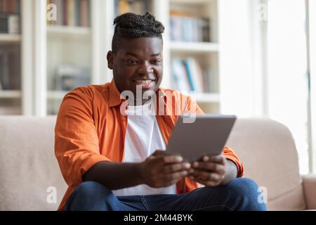 Positive cool black guy using digital tablet at home Stock Photo