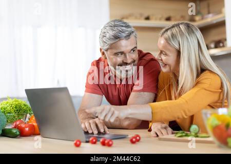 Cheerful mature couple looking for nice recipe on Internet Stock Photo
