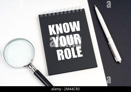 Business and economy concept. On a black and white surface lies a magnifying glass, a pen and a notepad with the inscription - Know Your Role Stock Photo