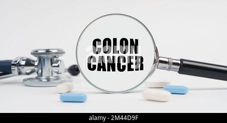Medicine and health concept. On a white surface lie pills, a stethoscope and a magnifying glass with the inscription - COLON CANCER Stock Photo