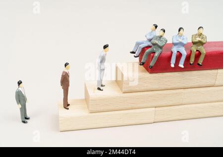 Corruption concept. Figures of people rise on wooden blocks. Figures of corrupt officials are sitting on the top of the red block. Stock Photo