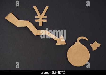 Concept of economic crisis. On a black surface is a graph with a down arrow, a yen symbol and a bomb. The symbol and arrow are made of cardboard Stock Photo