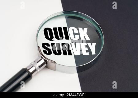 Business concept. On the surface, which is half black and white, lies a magnifying glass inside which is written - QUICK SURVEY Stock Photo