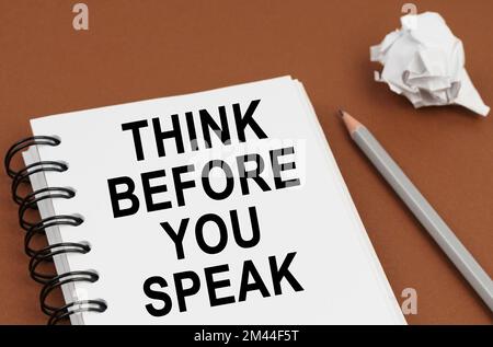 Business and finance concept. On a brown surface lies a pen, crumpled paper and a notepad with the inscription - THINK BEFORE YOU SPEAK Stock Photo