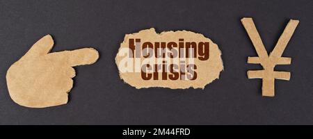 Economy and finance concept. On a black surface, a figure of a hand, a yen symbol and a torn cardboard with the inscription - Housing Crisis Stock Photo