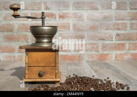Old manual coffee grinder. Brick wall as a background with scattered coffee beans on the table Stock Photo