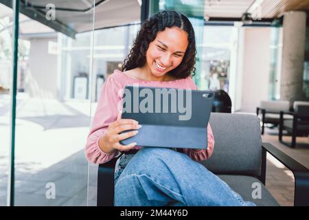 Happy young latin student woman using a tablet and sitting outside a cafe in her free time Stock Photo