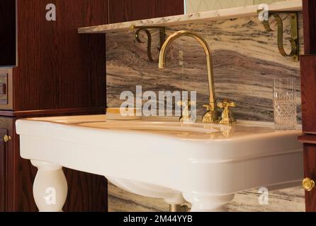 White antique style porcelain sink on legs with nuanced marble backsplash and brown stained vanity in guest bathroom inside contemporary home. Stock Photo