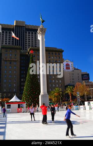 A small group of people ice skate on a winter day oin front of a large pillar and Christmas tree in Union Square in San Francisco Stock Photo