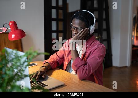 Tired African student guy feeling sleepy while studying online on laptop for long hours at home Stock Photo