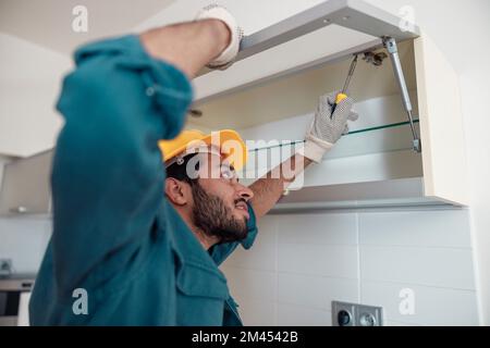 Close up of worker in uniform is assembling furniture on kitchen. Repair concept Stock Photo