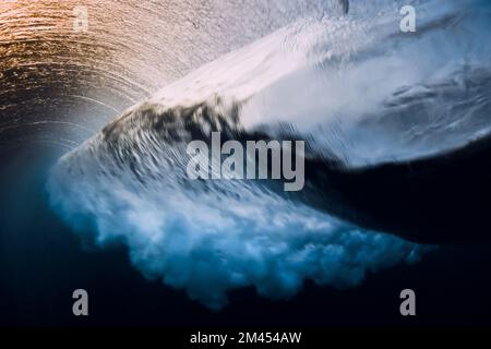 Barrel wave crashing in ocean with sunset or sunrise light. Underwater view of surfing wave Stock Photo