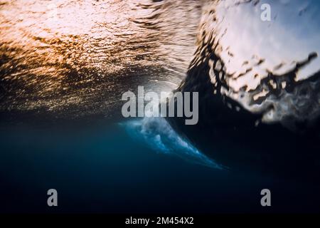Barrel wave crashing in ocean with sunset or sunrise light. Underwater view of surfing wave Stock Photo