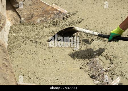 Shovel and cement. Shovel in hands of worker. Cement mixture spilled on road. Cleaning of building material. Working rowing. Stock Photo