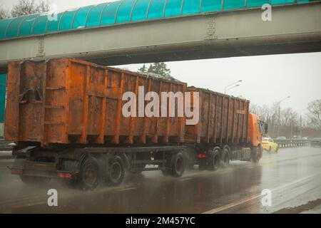 Truck with orange body. Big trailer. Transportation of waste. Fuel delivery. Passage under bridge. Rain on highway. Stock Photo
