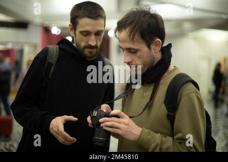 Guys look at photos. Men use camera. Two students learn to take photos. Young people at University. Stock Photo