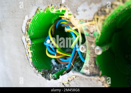 Multi-colored wires in a green socket under the socket on the facade of the house. Installed close-up mortgage for future electronics on the street in Stock Photo