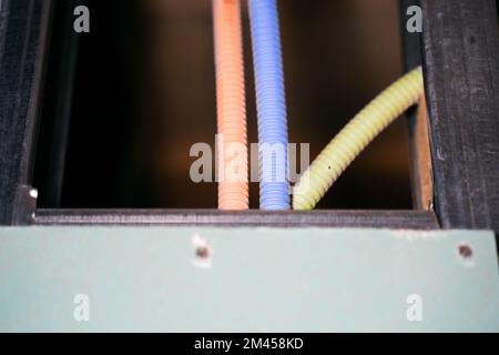 Red, blue and yellow corrugated pipes with wires come out of a metal profile inside a plasterboard wall. Distribution of wiring during repairs. Overhe Stock Photo