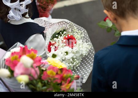 Flowers in hands of child. Bouquet of flowers for teacher. Details of holiday at school. School day. Flowers and children. Stock Photo