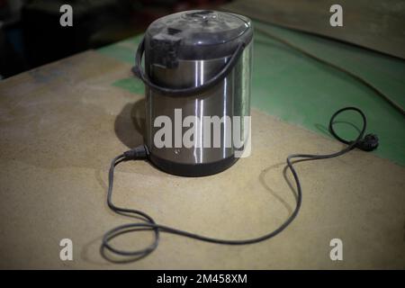 Old thermos. Electrical equipment on table. Boiler for warming water. Repair of electric kettle. Stock Photo