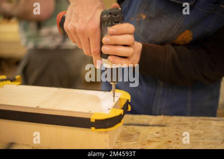 Hand holds box. Guy creates box out of wood. Work in workshop. Wood processing. Fixing template. Stock Photo
