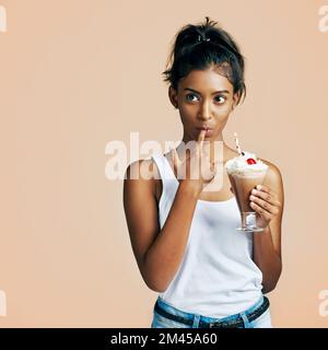 Dont waste a single drop. Studio shot of a beautiful young woman posing with a chocolate milkshake against an orange background. Stock Photo