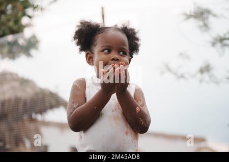 African-American child holding chicken egg with color stain on hand and dress. Stock Photo