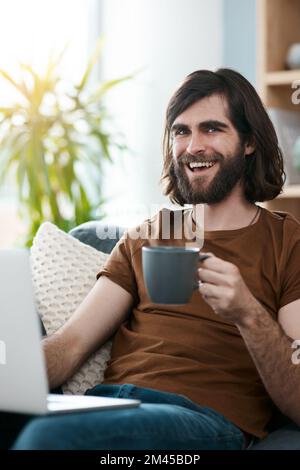 Dont mind me Im just over here blogging away. a handsome young man using his laptop while relaxing on a sofa in his living room. Stock Photo